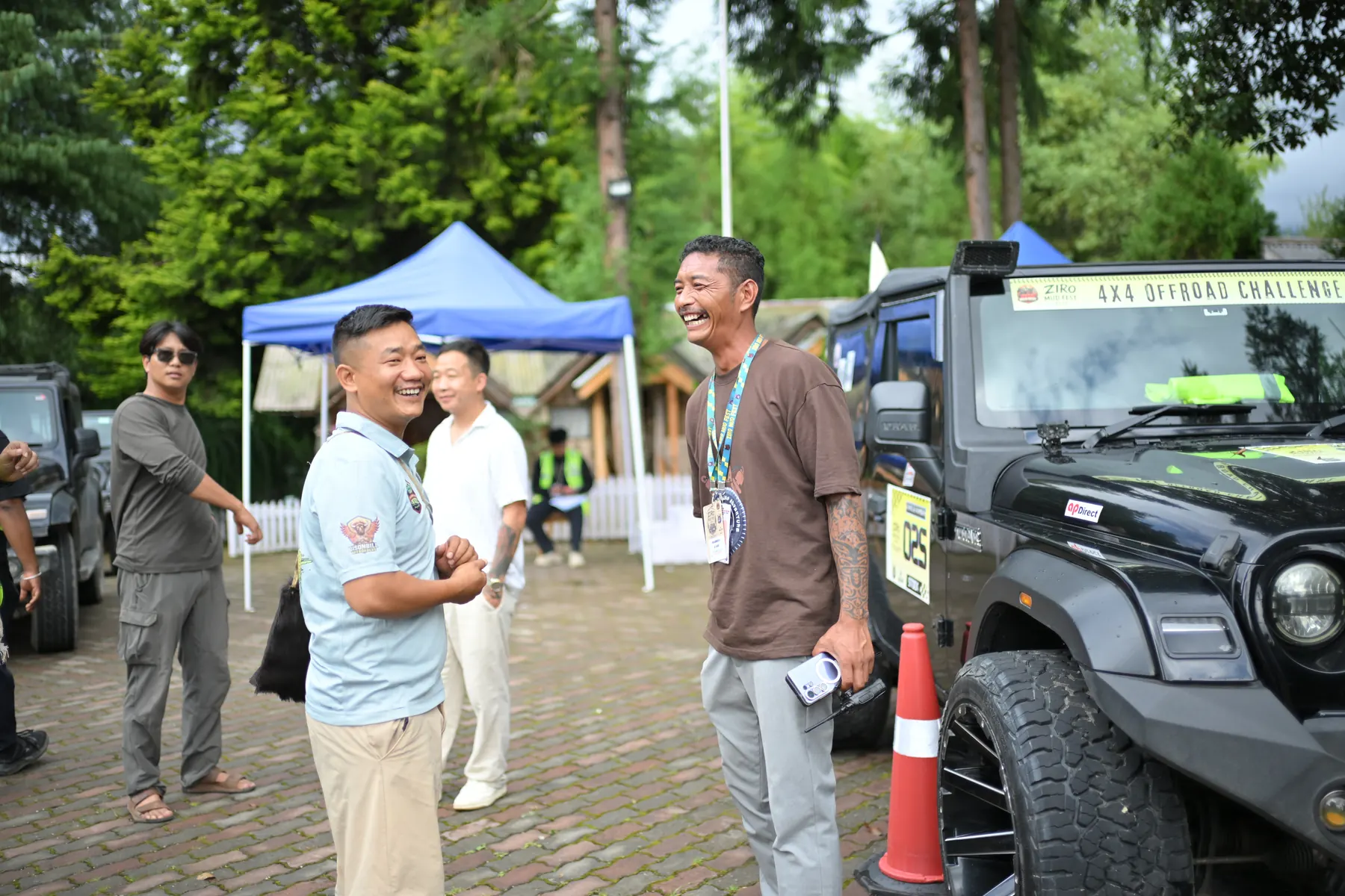 People talking beside a modified off-road vehicle and a blue canopy in the paddock.