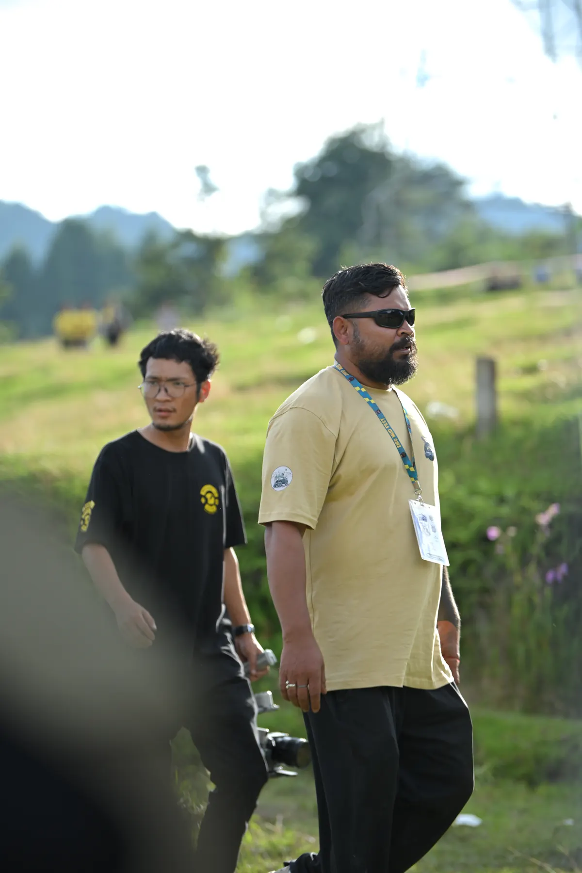 Two men wearing event lanyards walking across a grassy field.
