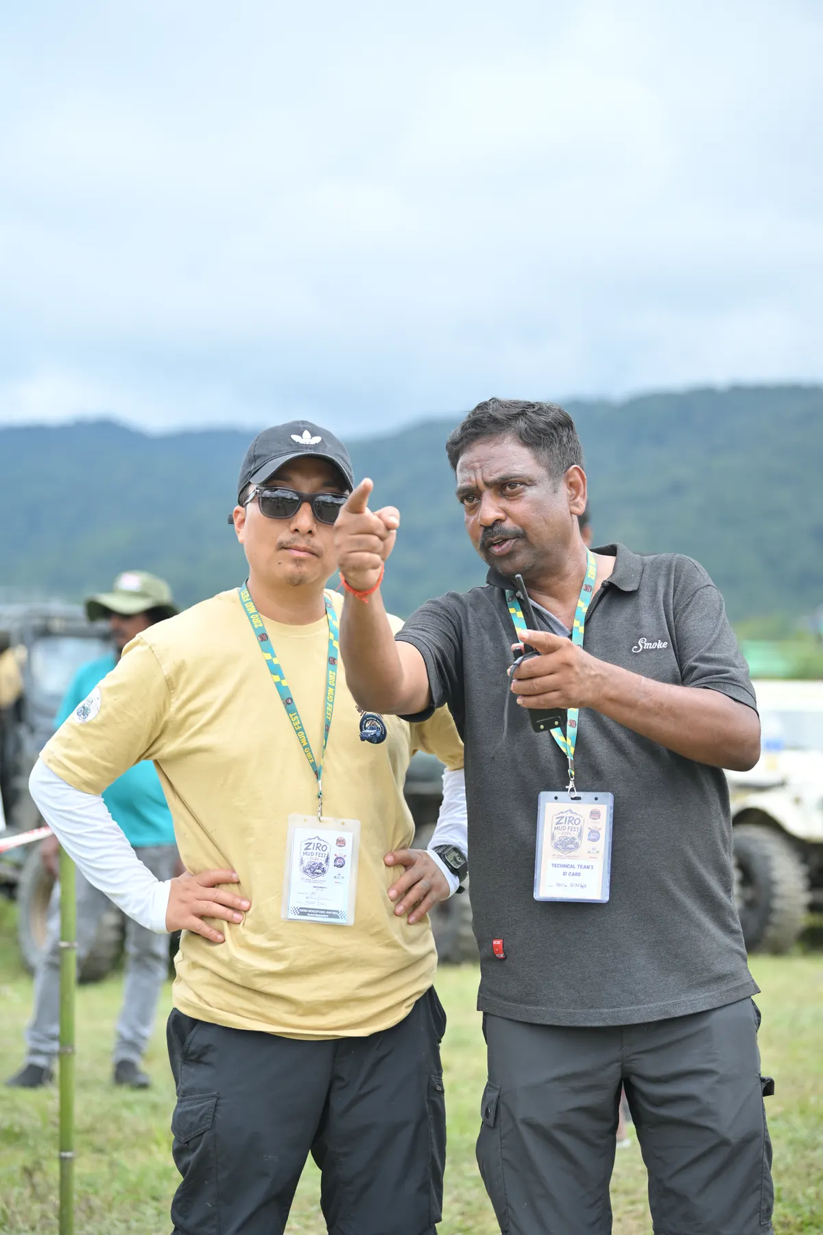 Two officials in event lanyards, one pointing out across the field.