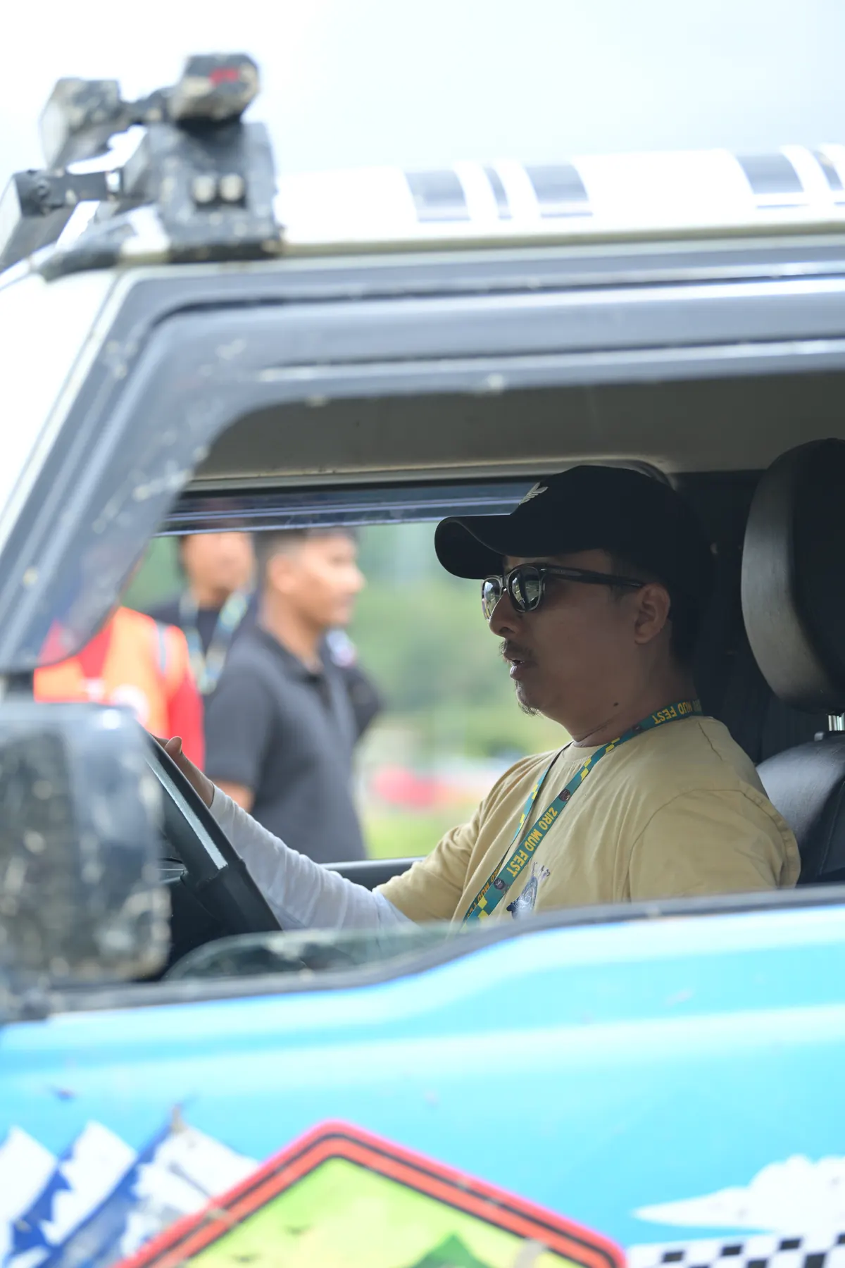 A driver in a cap at the wheel of a rally-liveried SUV.