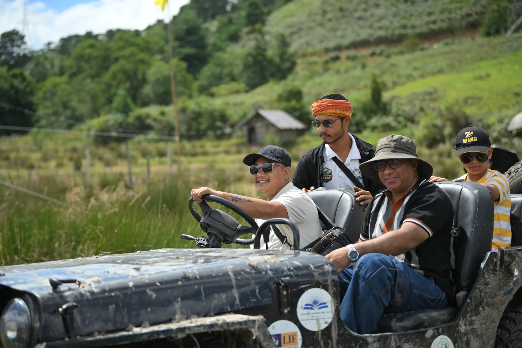 Two men laughing in an open, mud-spattered jeep.
