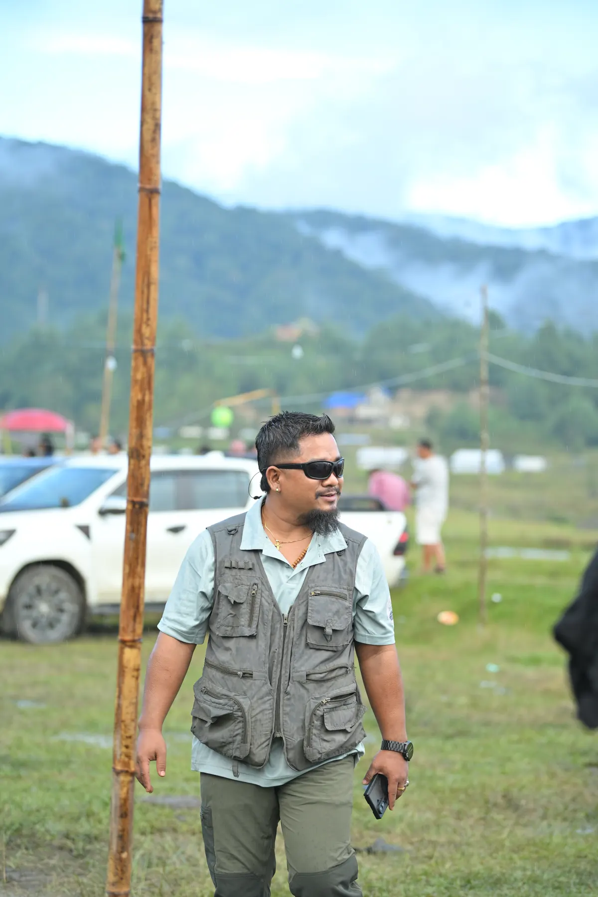 A man in a field vest walking across the ground, misty hills behind.