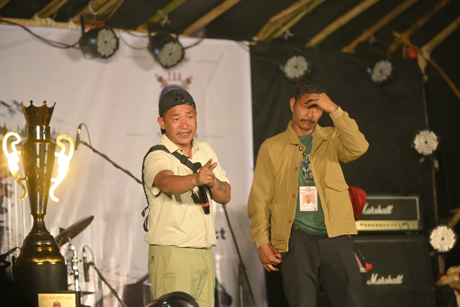 A man speaking into a microphone on stage beside a large trophy.