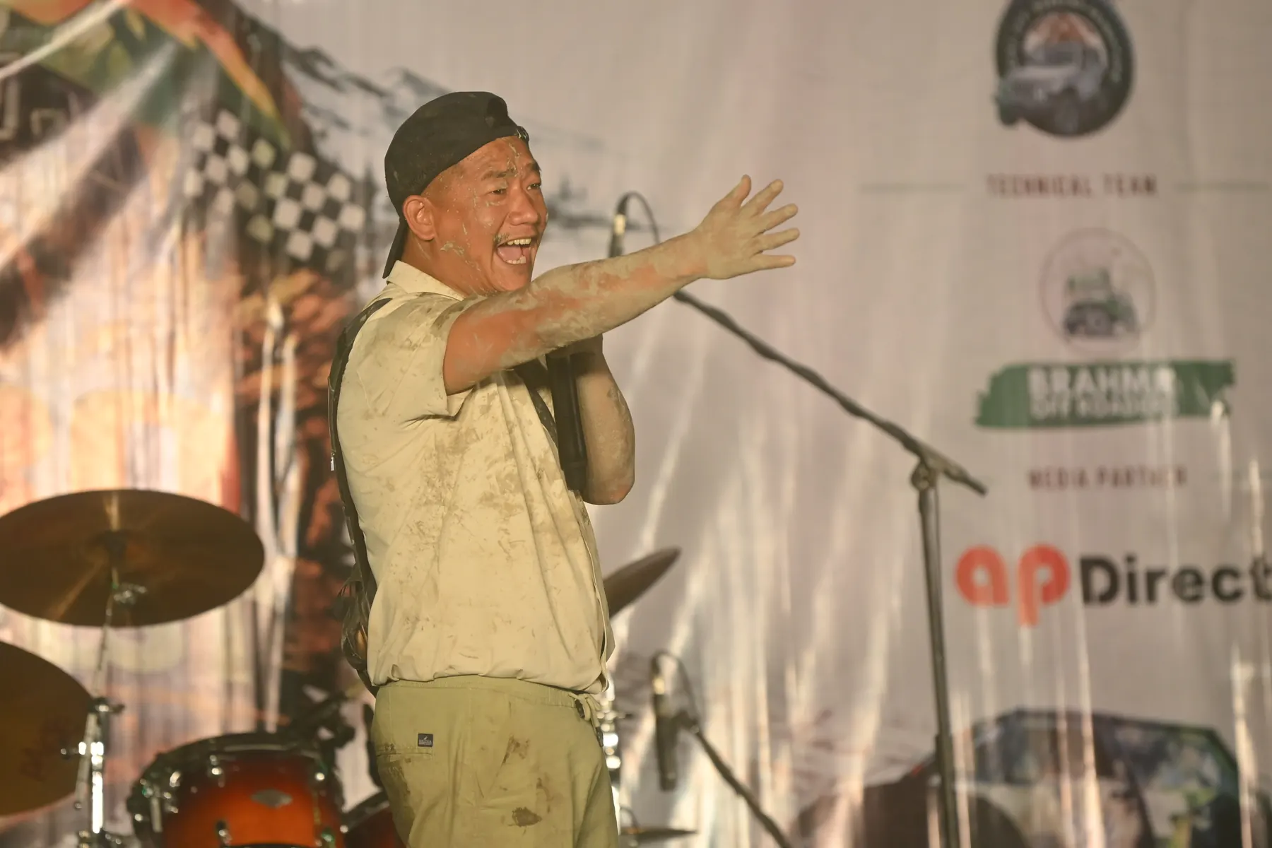 A man on stage gesturing to the crowd, a sponsor backdrop behind him.